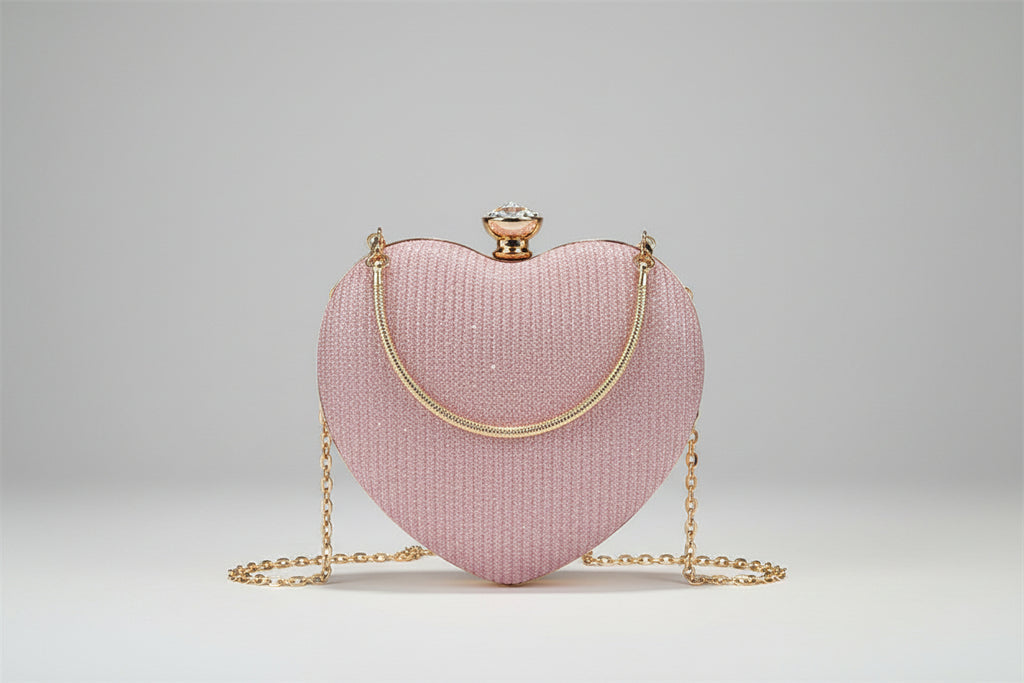 Pink heart-shaped handbag with gold chain held by a person on a dark surface.