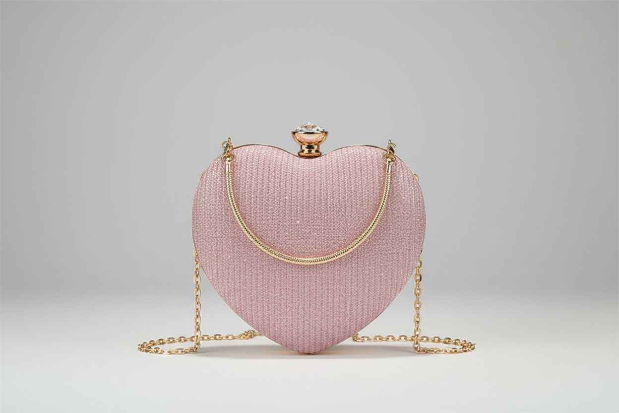 Pink heart-shaped handbag with gold chain held by a person on a dark surface.
