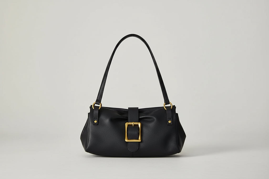 Black handbag with gold buckle held by a person wearing a brown sweater.